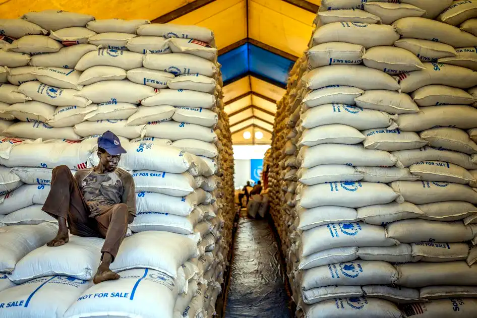 A worker sits atop sacks of food aid in a hangar where supplies are piling up because deliveries have halted because of the conflict at a World Food Programme (WFP) warehouse in Bor, Jonglei State, on February 13, 2026 ()© 2026 Luis Tato/AFP via Getty Images)