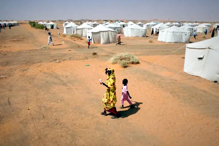 A woman and a child, displaced from North Darfur's capital, el-Fasher, or other conflict-affected areas, walk in the newly established el-Afadh camp in al-Dabba, in Sudan's Northern State, Sudan [Marwan Ali/AP]