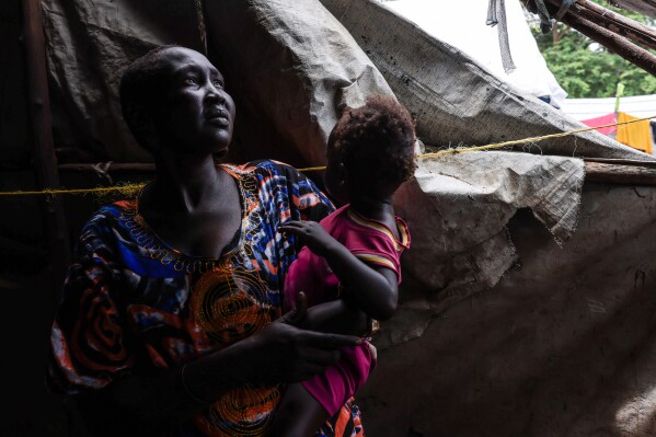 Rebekah Nyekhor, 31 years old, a mother of five, stands inside her makeshift home, carrying her child, in an IDP camp on the outskirts of Bor, South Sudan, Monday, Aug. 18, 2025. (AP Photo/Caitlin Kelly)