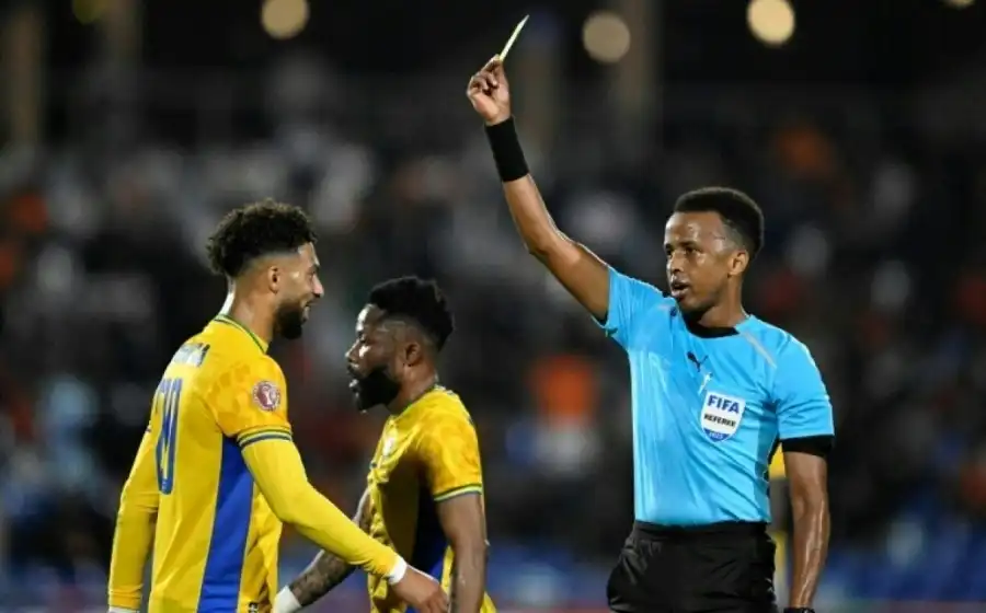 Somali referee Omar Artan shows a yellow card to Gabon's No. 20 striker, Denis Boanga, during the Africa Cup of Nations Group F match between Gabon and Ivory Coast at the Marrakech Grand Stadium on December 31, 2025 (© AFP)