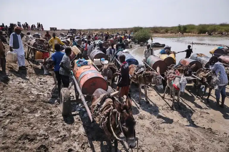 Sudanese refugees wait for their turn to get drinking water from a muddy pond in Gerbana